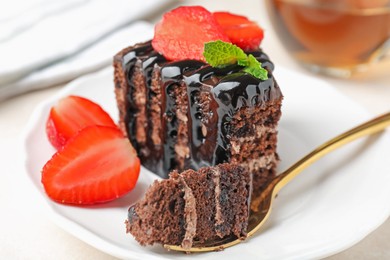 Photo of Piece of chocolate cake served with strawberries and spoon on white table, closeup