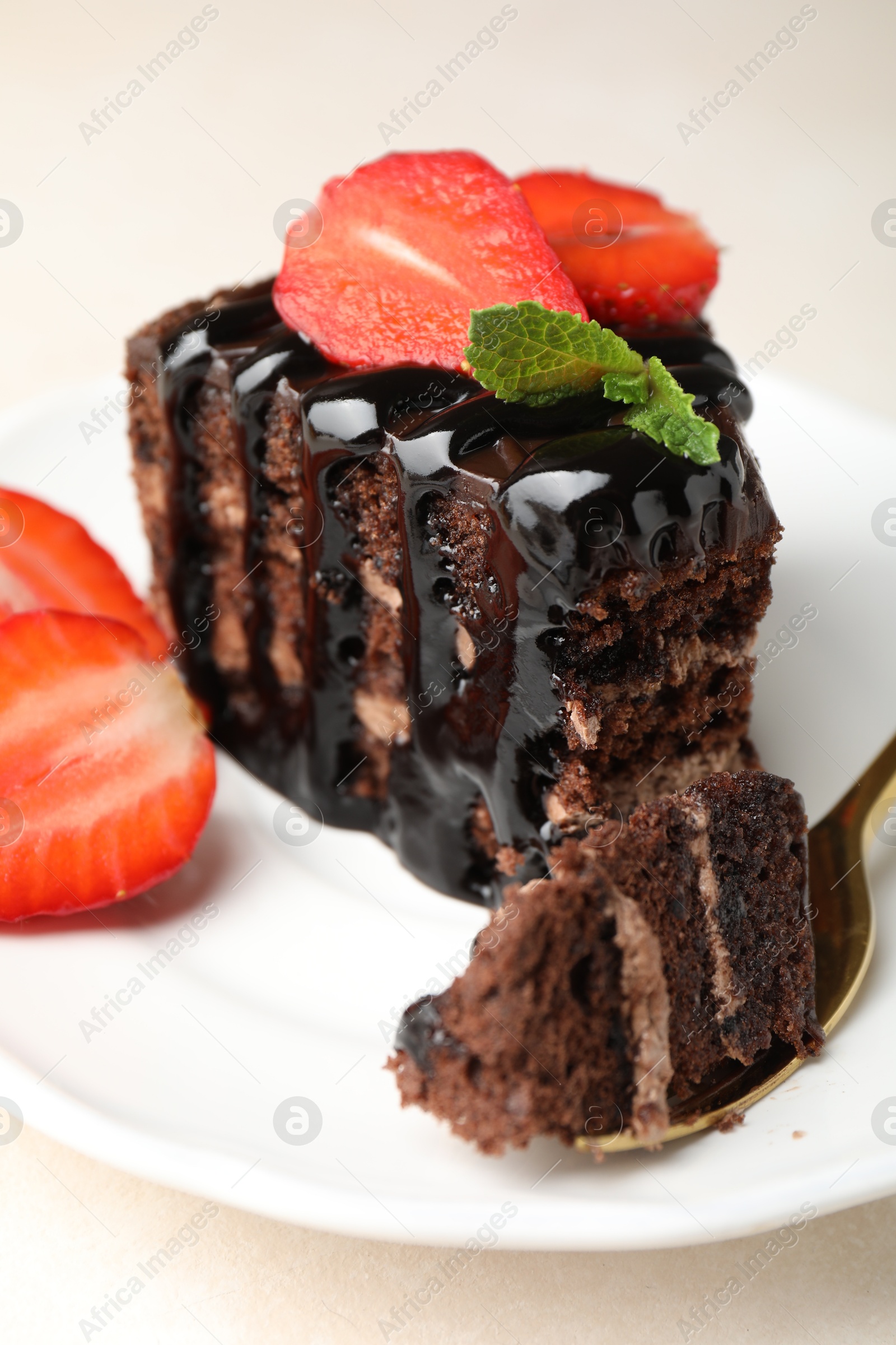 Piece of chocolate cake served with strawberries and spoon on white table, closeup Photo of Piece of chocolate cake served with strawberries and spoon on white table, closeup