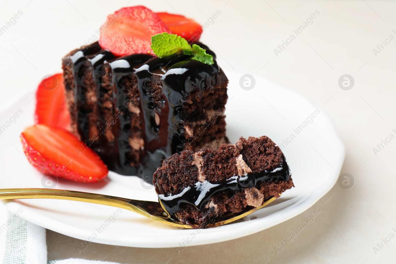 Piece of chocolate cake served with strawberries and spoon on white table, closeup Photo of Piece of chocolate cake served with strawberries and spoon on white table, closeup