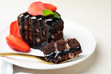 Photo of Piece of chocolate cake served with strawberries and spoon on white table, closeup