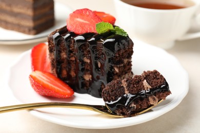 Photo of Piece of chocolate cake served with strawberries and spoon on white table, closeup