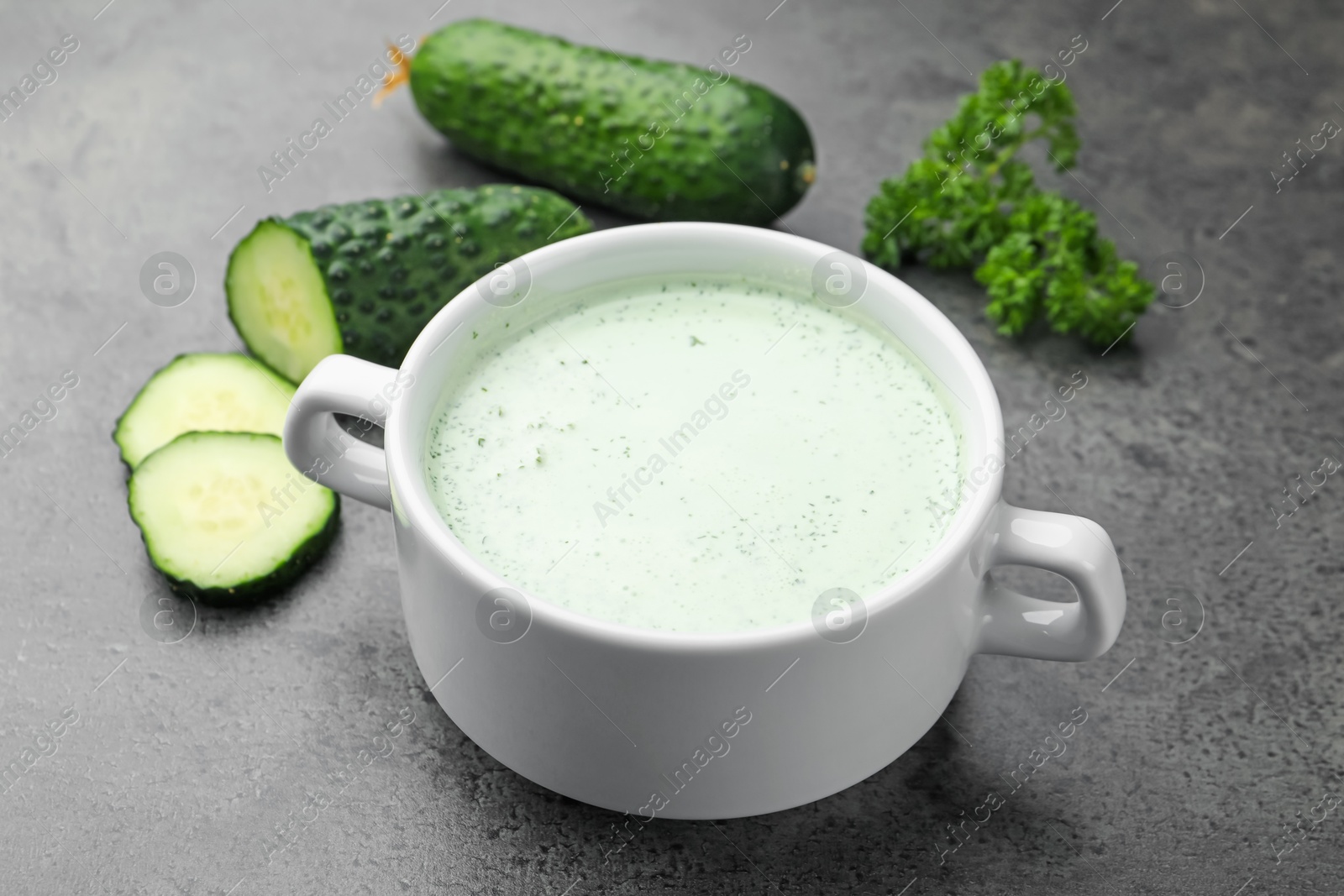 Photo of Tasty cucumber soup and fresh vegetables on grey table, closeup