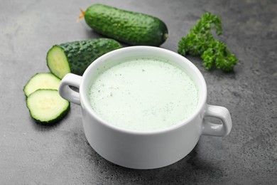 Photo of Tasty cucumber soup and fresh vegetables on grey table, closeup