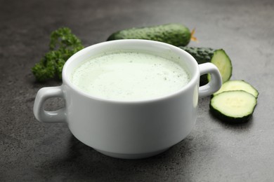 Photo of Tasty cucumber soup and fresh vegetables on grey table, closeup