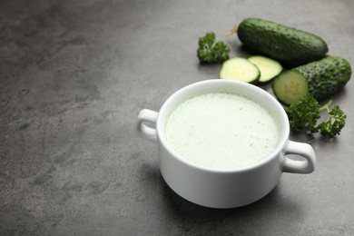 Photo of Tasty cucumber soup and fresh vegetables on grey table, closeup. Space for text