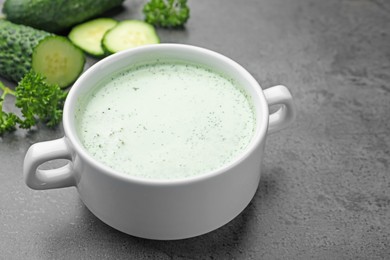 Photo of Tasty cucumber soup and fresh vegetables on grey table, closeup