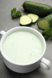Photo of Tasty cucumber soup and fresh vegetables on grey table, closeup