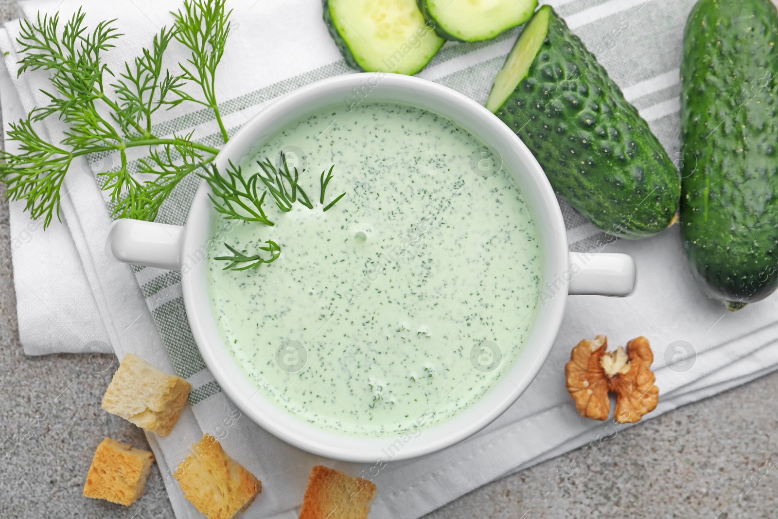 Photo of Tasty cucumber soup with dill, croutons, walnuts and vegetables on grey table, flat lay