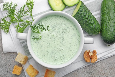 Photo of Tasty cucumber soup with dill, croutons, walnuts and vegetables on grey table, flat lay