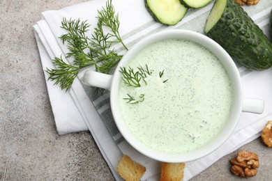 Photo of Tasty cucumber soup with dill, croutons, walnuts and vegetables on grey table, flat lay