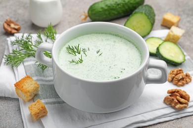 Photo of Tasty cucumber soup with dill, croutons, walnuts and vegetables on grey table, closeup