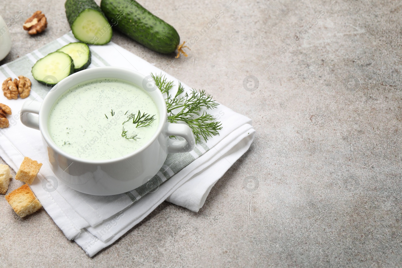 Photo of Tasty cucumber soup with dill, croutons, walnuts and vegetables on grey table. Space for text