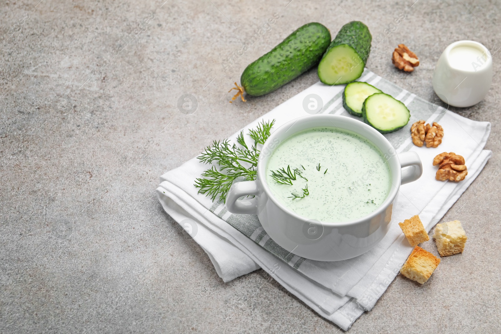 Photo of Tasty cucumber soup with dill, croutons, walnuts and vegetables on grey table. Space for text