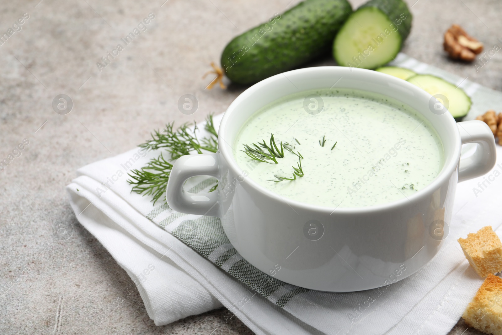 Photo of Tasty cucumber soup with dill, croutons, walnuts and vegetables on grey table, closeup