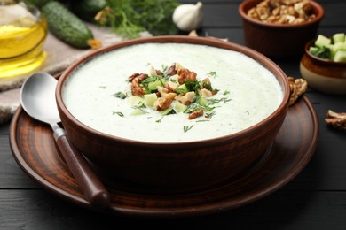 Photo of Tasty cucumber soup with dill and walnuts served on black wooden table, closeup