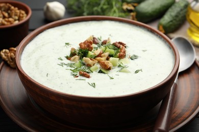 Photo of Tasty cucumber soup with dill and walnuts served on black wooden table, closeup
