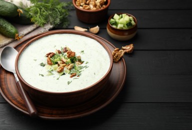Photo of Tasty cucumber soup with dill and walnuts served on black wooden table, closeup