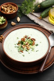Photo of Tasty cucumber soup with dill and walnuts served on black wooden table, closeup