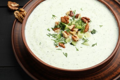 Photo of Tasty cucumber soup with dill and walnuts on black wooden table, closeup