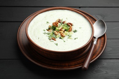 Photo of Tasty cucumber soup with dill and walnuts served on black wooden table, closeup