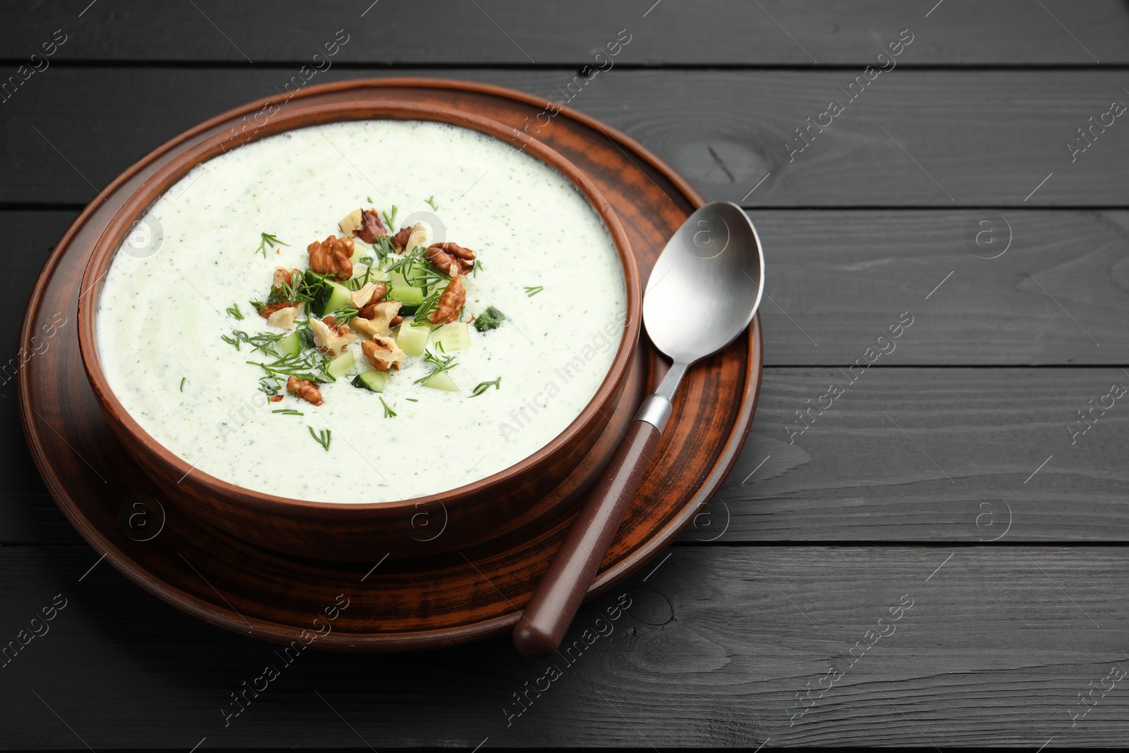 Photo of Tasty cucumber soup with dill and walnuts served on black wooden table, closeup. Space for text