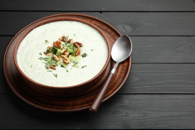 Photo of Tasty cucumber soup with dill and walnuts served on black wooden table, closeup. Space for text