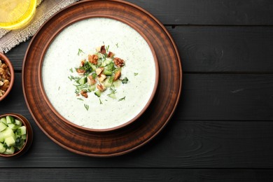 Photo of Tasty cucumber soup with dill and walnuts on black wooden table, top view