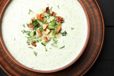 Photo of Tasty cucumber soup with dill and walnuts on black wooden table, top view