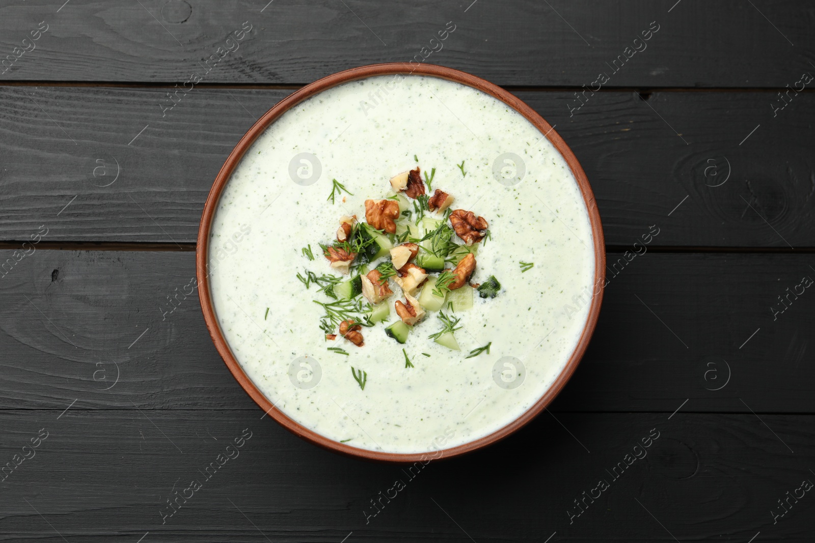 Photo of Tasty cucumber soup with dill and walnuts on black wooden table, top view