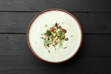Photo of Tasty cucumber soup with dill and walnuts on black wooden table, top view