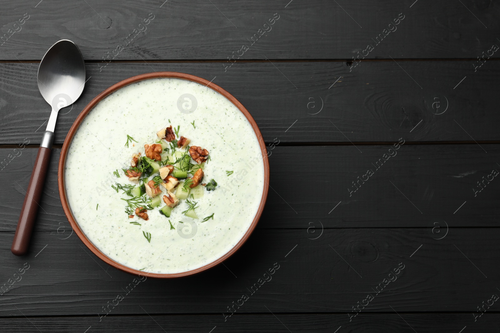 Photo of Tasty cucumber soup with dill and walnuts served on black wooden table, top view. Space for text