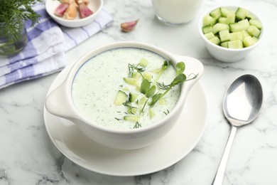 Photo of Tasty cucumber soup with dill and microgreens served on white marble table, closeup