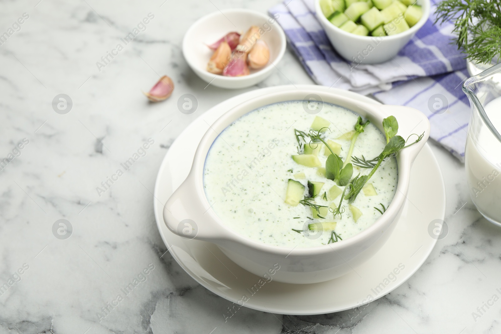 Photo of Tasty cucumber soup with dill, microgreens and ingredients on white marble table, closeup