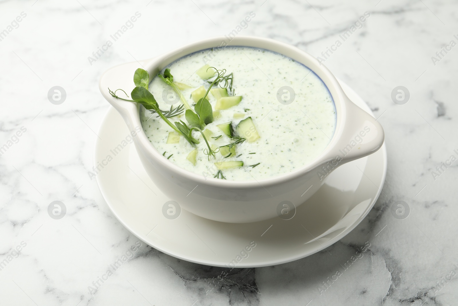 Photo of Tasty cucumber soup with dill and microgreens on white marble table, closeup