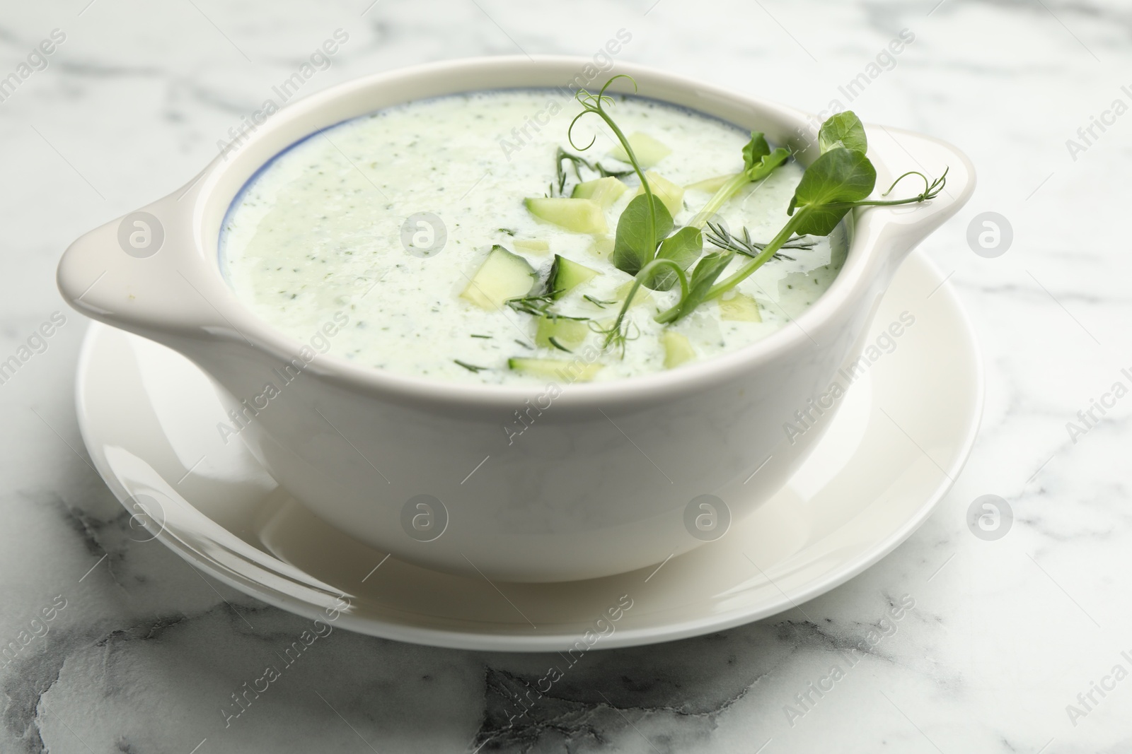 Photo of Tasty cucumber soup with dill and microgreens on white marble table, closeup