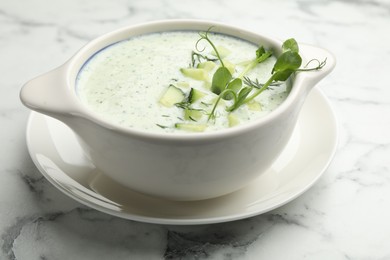 Photo of Tasty cucumber soup with dill and microgreens on white marble table, closeup