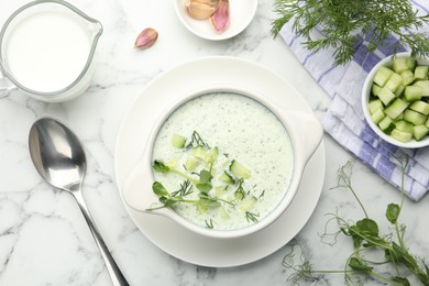 Photo of Tasty cucumber soup with dill and microgreens served on white marble table, flat lay