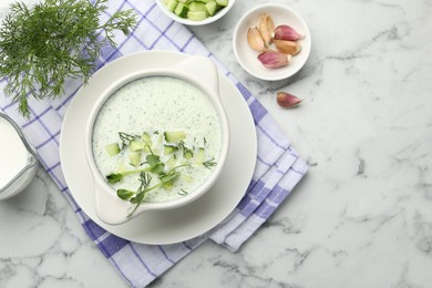 Photo of Tasty cucumber soup with dill, microgreens and ingredients on white marble table, flat lay