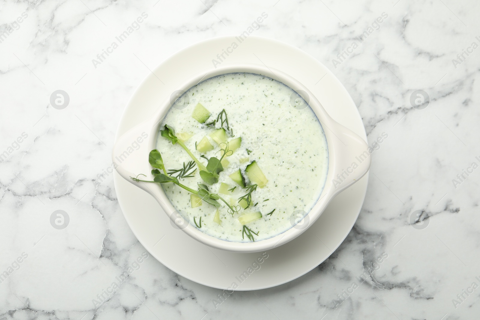 Photo of Tasty cucumber soup with dill and microgreens on white marble table, top view