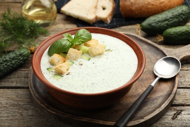 Photo of Tasty cucumber soup with croutons and basil served on wooden table, closeup