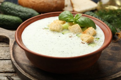 Photo of Tasty cucumber soup with croutons, basil, bread and vegetables on wooden table, closeup