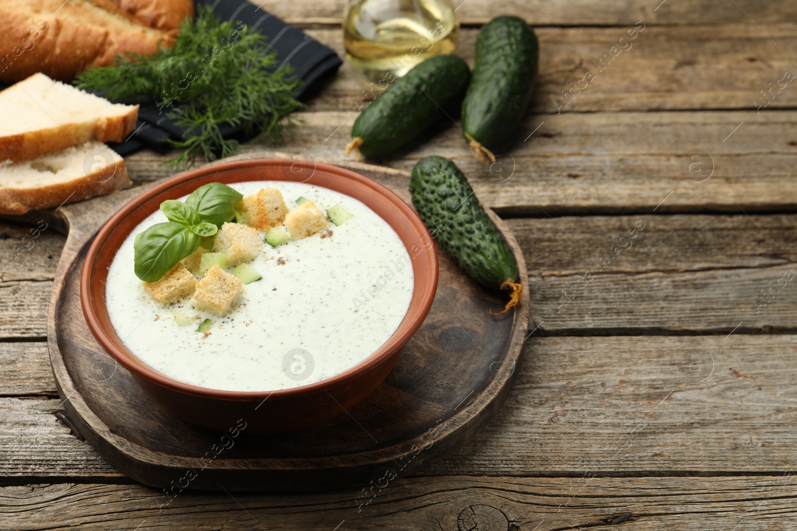 Tasty cucumber soup with croutons, basil, bread and vegetables on wooden table Photo of Tasty cucumber soup with croutons, basil, bread and vegetables on wooden table