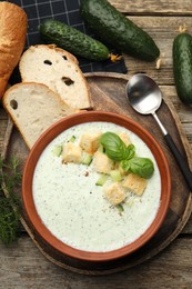 Photo of Tasty cucumber soup with croutons and basil served on wooden table, flat lay