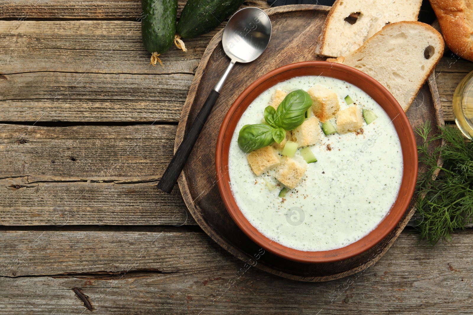 Photo of Tasty cucumber soup with croutons and basil served on wooden table, top view. Space for text