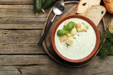 Photo of Tasty cucumber soup with croutons and basil served on wooden table, top view. Space for text