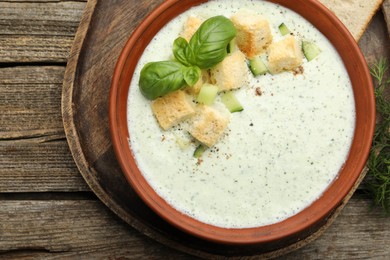 Photo of Tasty cucumber soup with croutons and basil on wooden table, top view