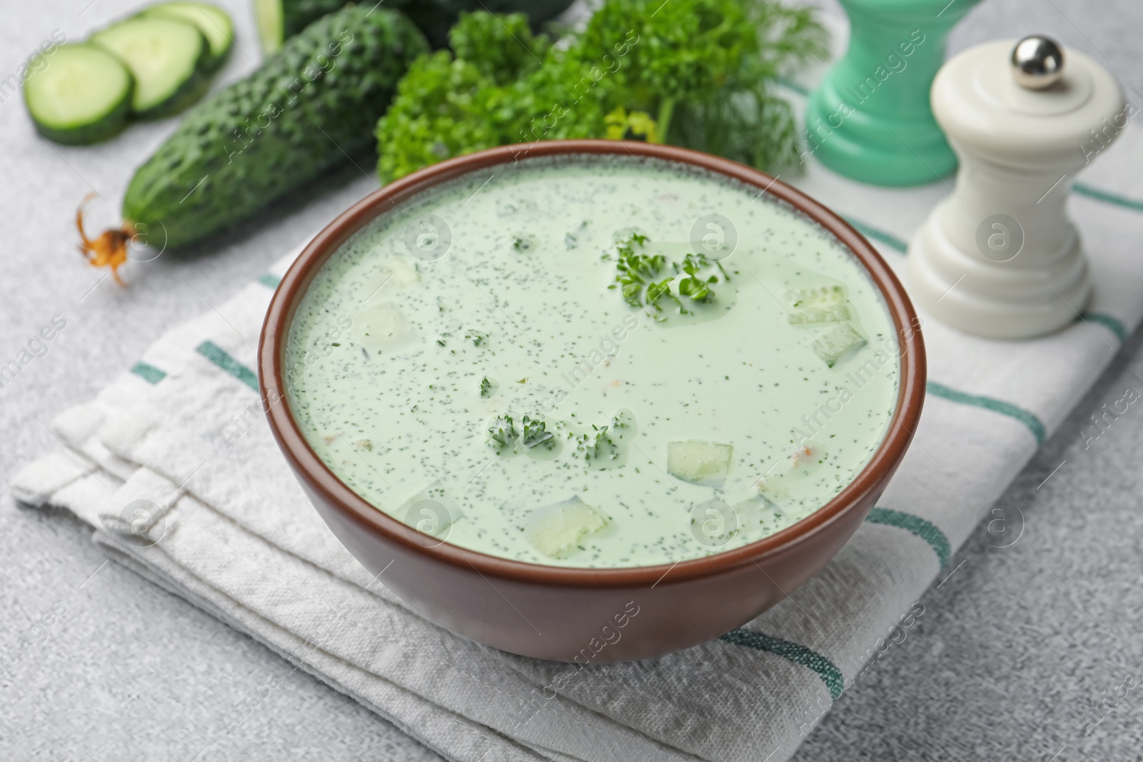 Photo of Tasty cucumber soup and ingredients on light grey table, closeup