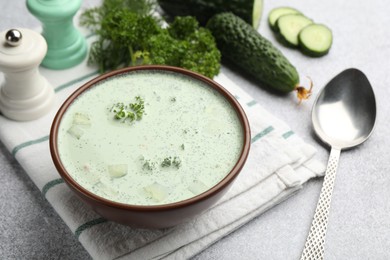 Photo of Tasty cucumber soup, spoon and ingredients on light grey table, closeup