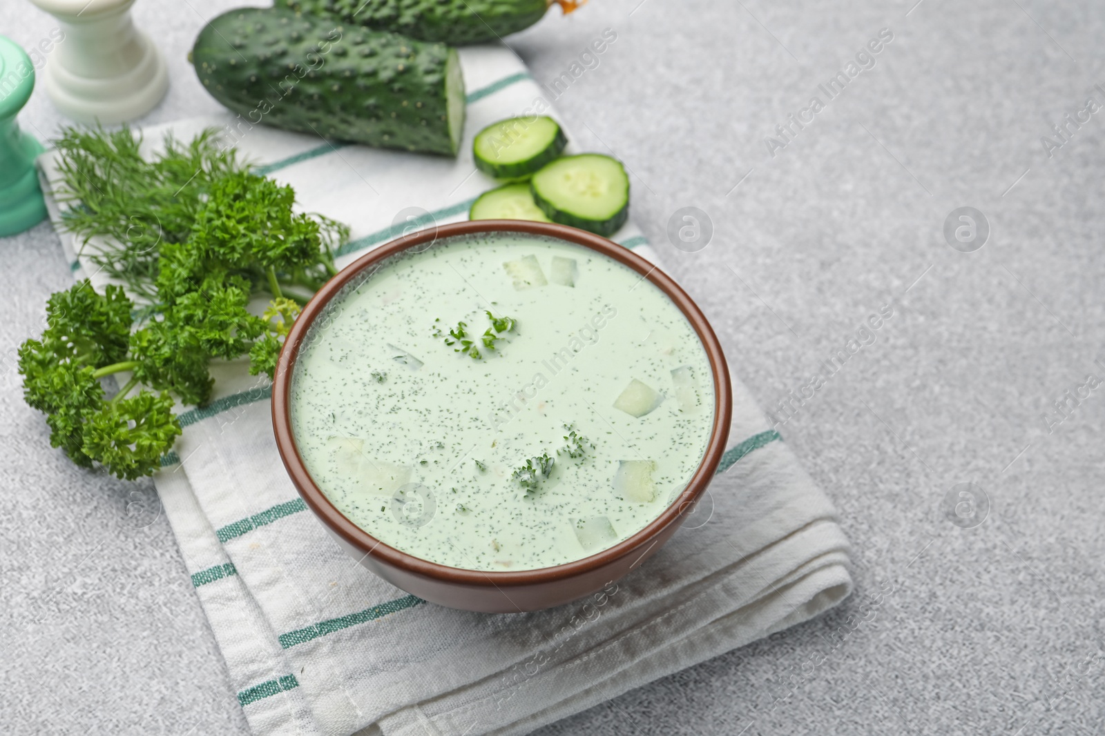 Photo of Tasty cucumber soup and ingredients on light grey table. Space for text