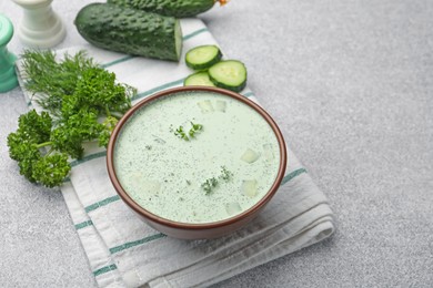 Photo of Tasty cucumber soup and ingredients on light grey table. Space for text